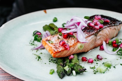 En bit grillad lax med sparris och granatäpple-kärnor på en tallrik